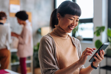 Young Asian business woman smiling while using phone in busy office.