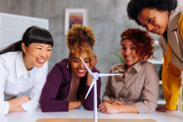 Four multiracial business women looking at windmill model happy about eco project success.