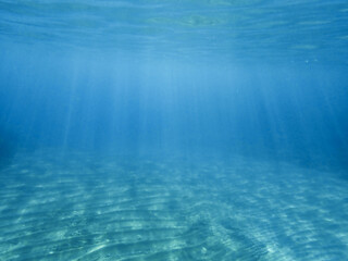 Fototapeta premium Dark blue ocean surface seen from underwater. Abstract waves underwater and rays of sunlight shining through, Sun light rays undersea deep, Underwater background with sea bottom, Mediterranean sea.
