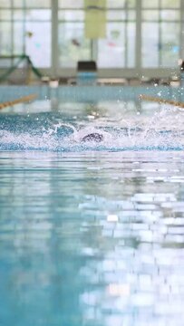 Successful professional female swimmer swimming butterfly stroke in the indoor lap pool, front view slow motion. Concept of determination and hard sports training.
