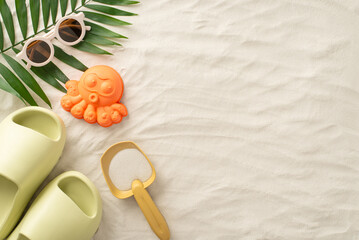 Discover the joy of a summer getaway with children by the sea: Above view picture featuring sand toys for children, palm leaf, sunglasses and slippers on isolated sandy background with copyspace