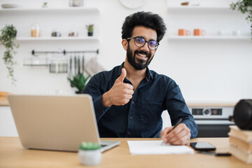 Portrait of attractive indian businessman posing at office desk with digital devices in spacious...
