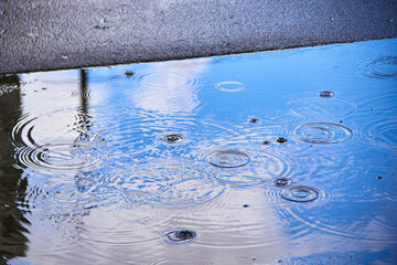 a puddle on the asphalt with a reflection of the blue sky during when it rains.