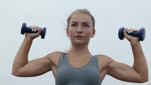 Strong fit young woman performing shoulder press with dumbbells.