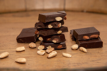 Close-up of delicious pieces of dark chocolate with almonds forming a tower on a wooden table.