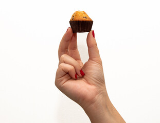 Close-up of a woman's hand with red fingernails holding a mini chocolate chip cupcake on a white...