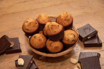 Close-up of a wooden table full of desserts and pastries, chocolate chip muffins on a wicker basket surrounded by chocolate towers with almonds.