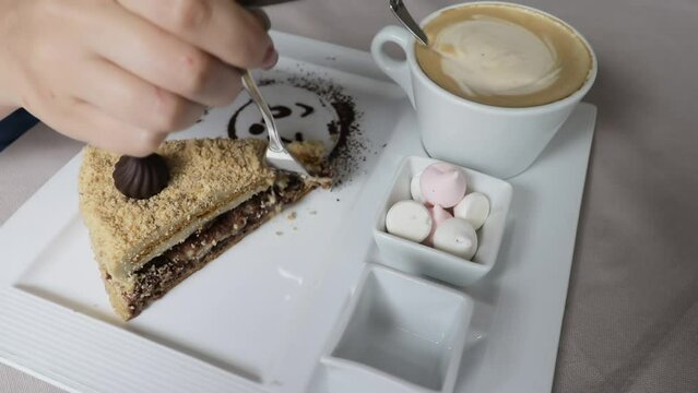 Woman hand with fork take a piece of cace from the plate, cappuccino foam in cup