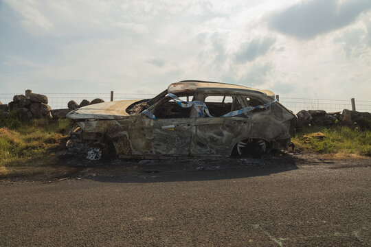 Scene Of An Auto Accident With Police Tape On A Burnt Car Wreck On A Country Road In The Lomond Hills Regional Park, Fife, Scotland, UK.