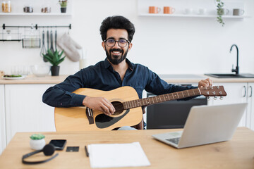 Portrait of handsome bearded adult posing with six-string guitar while enjoying pleasant pastime at...