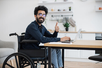 Close up view of smiling wheelchair user typing on portable computer while staying in distant workplace. Cheerful professional performing business project while doing full-time job from home.