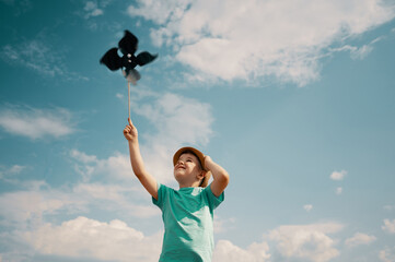 Little boy holds handcrafted windmill pinwheel in hand against the background of sky and clouds	
