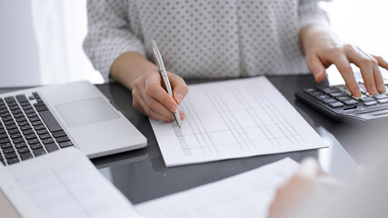 Woman accountant using a calculator and laptop computer while counting taxes with a client or a colleague. Business audit team, finance advisor