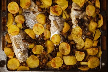 oven grilled sea bream fish with delicious curry sauce served on baking tray, baked potatoes with...