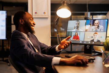 Smiling executive manager having remote conversation with team discussing marketing strategy during online videocall meeting. Diverse coworkers working at company growth report in office