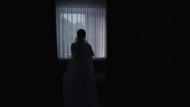 Silhouette of a Beautiful sexy Bride girl posing through the window. Slow motion