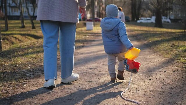 Happy family outdoor. Back view of mother and her child on walk in park. Mom holding baby hand walking with child son outdoor. Unrecognizable no face woman little baby boy resting walking in nature
