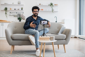 Front view of cheerful content maker in casual wear recording video to followers on modern...