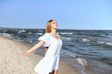 Fototapeta na wymiar Happy smiling beautiful woman is on the ocean beach in a white summer dress, open arms