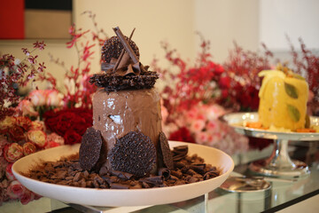 Uma magnífica torre de sorvete de chocolate, majestosamente servida na mesa de um evento sofisticado. A mesa se destaca, decorada com flores em tons suaves de rosa, adicionando um toque de elegância 