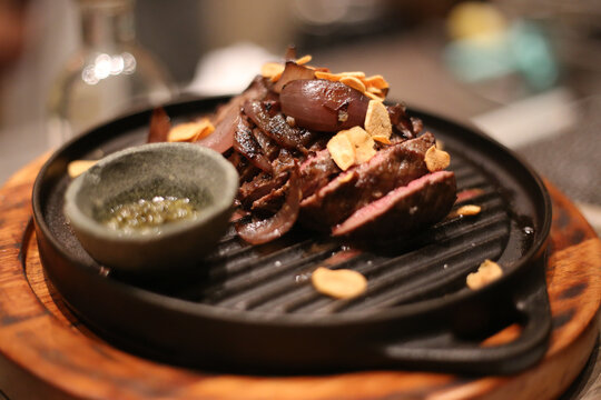  Suculentas fatias de carne nobre grelhadas na brasa, servidas em charmosas chapas de ferro, acompanhadas de lascas de alho e cebolas douradas, e um potinho de molho irresist&iacute;vel.