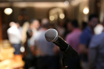 Um microfone posicionado em primeiro plano, aguardando ansiosamente o início do show em um evento social.