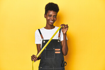 African tailor woman with measuring tape, yellow studio background.