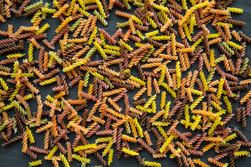 Assortment of different kinds of rotini pasta on black background, top view. 