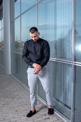 a stylish man in light pants and a black shirt against the background of empty walls holds glasses in his hands and looks away angrily