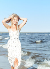 Happy blonde beautiful woman having fun on ocean beach while dancing in waves