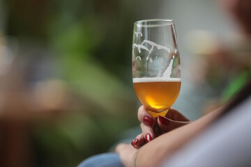 Mão feminina segurando uma taça de cerveja em um evento social animado.