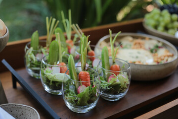 Uma salada fresca e colorida, cuidadosamente servida em potes de vidro, destacando-se pela presença das mini cenouras com seus talos verdes intactos. Um toque especial em um evento social chique, dura