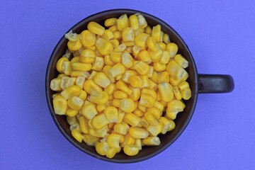 yellow corn food in a brown ceramic cup stands on a lilac table