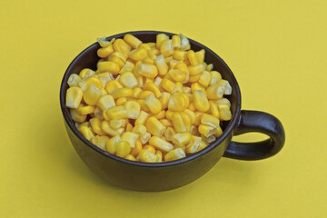 corn food in a brown ceramic cup stands on a yellow table