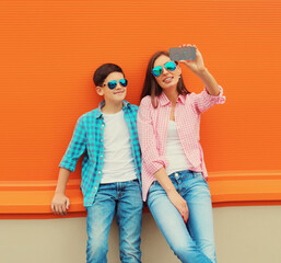 Happy smiling mother with son teenager taking selfie with smartphone on orange background