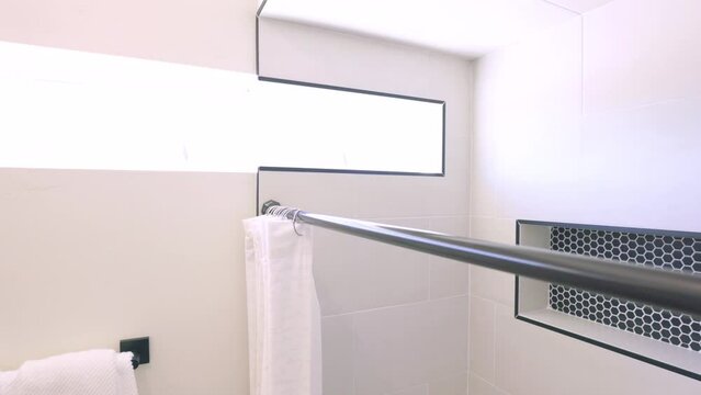 Move Along Bathroom Shower Curtain Rod Toward Window. slow motion view high angle moving along a shower curtain rod towards a unique window