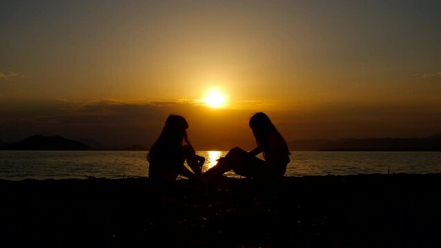 Two resting girl silhouette against sunset. A view of two resting children silhouette on the luxury beach by the sea in summer.