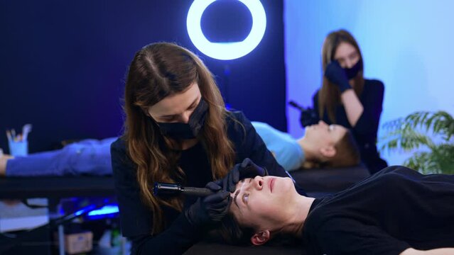 Modern beauty salon with professionals working on clients. Professionals performing the procedure of permanent eyebrow make up.