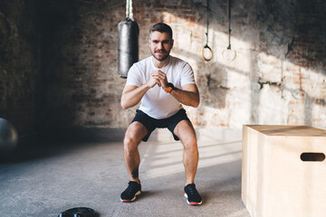Strong male athlete squatting at gym during fitness workout