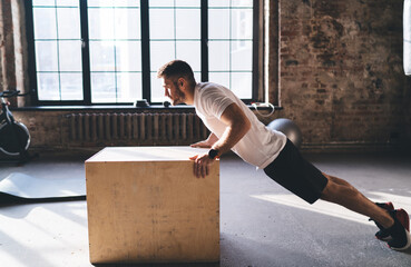 Strong sportsman doing workout with wooden box in gym