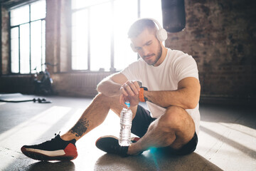 Concentrated sportsman in headphones checking fitness tracker indicators after training