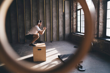 Focused man doing jumps on box in gym
