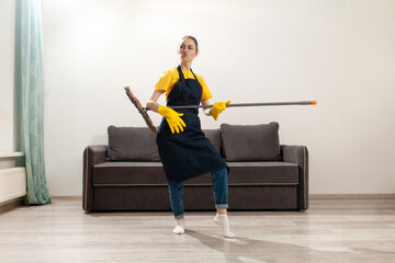 cheerful housekeeper in apron and gloves cleans houses and dances with mop, woman housewife washes the floor
