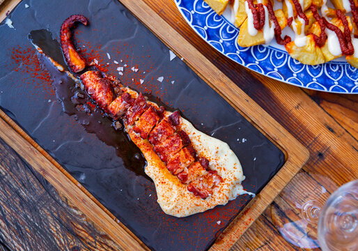 Spicy grilled octopus tentacle with potato parmentier on slate serving board. Traditional Spanish cuisine