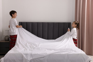 Brother and sister changing bed linens together in bedroom