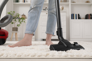 Woman cleaning carpet with vacuum cleaner at home, closeup