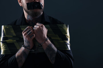 Taped up and handcuffed man taken as hostage on dark background, closeup. Space for text - obrazy, fototapety, plakaty