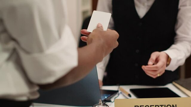 Close up of receptionist handing card key to african american tourist during check in process. Business travelling guest ready to enjoy hotel stay after receiving room access