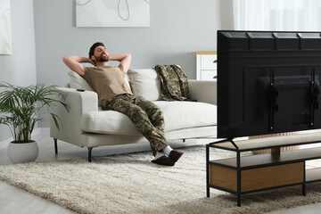 Soldier napping on soft sofa near TV in living room. Military service