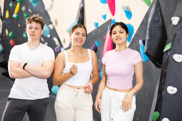 Two young women in sportswear and teen guy posing against training wall at climbing wall - Powered by Adobe